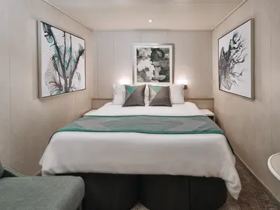 Moderne Innenkabine an Bord der Norwegian Sky mit Doppelbett, grüner Tagesdecke und grauen Kissen. Die hellen Wände zeigen drei abstrakte Kunstwerke.