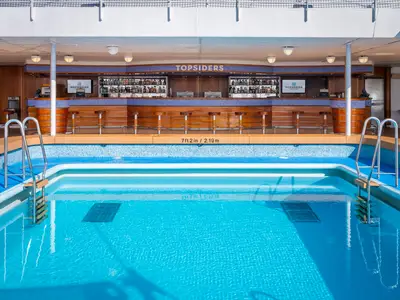 Blick auf die Topsiders Poolbar an Bord der Norwegian Sky. Im Vordergrund ein strahlend blauer Pool mit Einstiegsleitern. Dahinter die hölzerne Bar mit Hockern und Getränken.