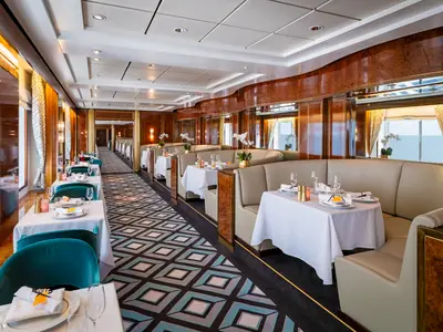 Blick in das elegante Spezialitätenrestaurant Le Bistro an Bord der Norwegian Sky mit festlich gedeckten Tischen, beigen Sitzbänken und großen Fenstern zum Meer. Ohne Personen.