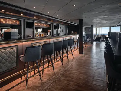 Der Barbereich "The Local" an Bord der Norwegian Sky zeigt eine lange Theke mit modernen Barhockern. Im Hintergrund sind raumhohe Fenster mit Meerblick zu sehen.