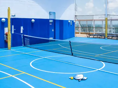 Ein blauer Multisportplatz auf dem Außendeck der Norwegian Sky. Es gibt ein Netz für Pickleball/Volleyball, Spielfeldlinien und Basketbälle. Ein Schutznetz sichert den Bereich.
