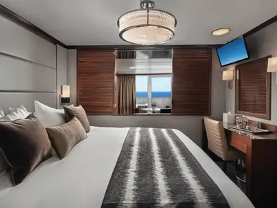 Moderne Suite an Bord der Norwegian Sky. Komfortables Doppelbett, Schreibtisch und TV. Der private Balkon bietet Meerblick und eine Sitzgruppe.