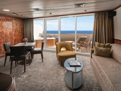 Eine geräumige Suite an Bord der Norwegian Sky mit einem eleganten Wohnbereich, Essplatz und Blick auf das Meer. Auf dem privaten Balkon ist ein Whirlpool zu sehen.