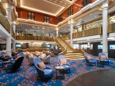 Das mehrstöckige Atrium der Norwegian Spirit zeigt eine goldene Treppe, bequeme blaue und beige Sessel, Rezeption und Balustraden. Ohne Personen.