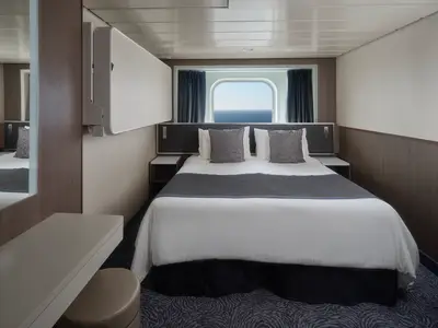 Helle Aussenkabine an Bord der Norwegian Spirit mit Doppelbett, grauen Kissen. Grosses Fenster mit Blick auf das weite Meer. Moderne, gemütliche Einrichtung.