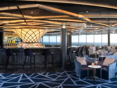 Die Spinnaker Lounge Bar an Bord der Norwegian Spirit. Eine moderne Bar mit samtigen Sesseln und Tischen. Grosse Fenster mit Meerblick. Dekorative Decke und Teppich.
