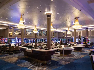 Casino an Bord der Norwegian Spirit mit eleganten Spieltischen, Barhockern und zahlreichen Spielautomaten. Opulente Kronleuchter und eine funkelnde Decke.