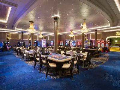 Das elegante Casino an Bord der Norwegian Spirit. Moderne Spieltische und Slot Machines, dazu funkelnde Deckenlichter, Kronleuchter und Säulen. Blauer Teppich mit Muster.