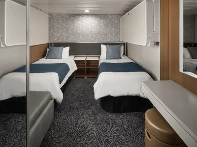 Helle Innenkabine an Bord der Norwegian Spirit mit zwei Einzelbetten. Weisse Bettwaesche, blaue Deckenlaeufer und moderne Moebel.