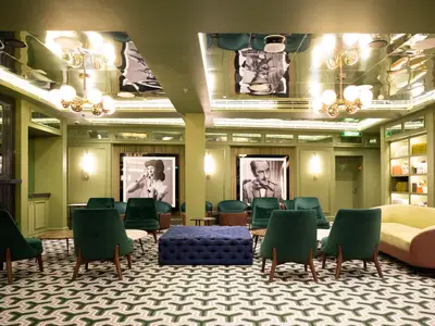 Elegante Lounge an Bord der Norwegian Spirit. Gruene Samtsessel, blauer Ottoman und grosse Schwarz-Weiss-Porträts schmuecken den Raum. Verspiegelte Decke mit Lichtern. Ein gemuetlicher Treffpunkt.