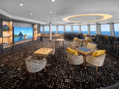Helle und moderne Lounge an Bord der Norwegian Spirit mit grossen Fenstern und Meerblick. Gemuetliche Sessel, Spieltische und beleuchtete Buecherregale sind zu sehen.