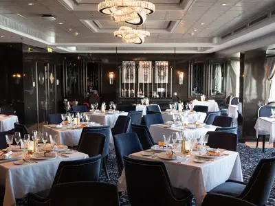 Blick in das elegant beleuchtete Spezialitätenrestaurant Le Bistro an Bord der Norwegian Spirit, mit zahlreichen gedeckten Tischen und blauen Samtstühlen.