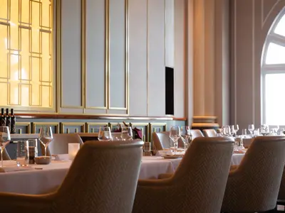 Blick ins elegante Hauptrestaurant an Bord der Norwegian Spirit. Mehrere Tische sind mit weissen Tischtüchern, Weingläsern, Wassergläsern und Wein gefüllt. Im Hintergrund eine grosse Fensterfront mit Tageslicht. Die Einrichtung ist modern und gediegen.