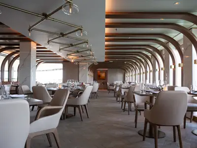 Ein elegantes Restaurant an Bord der Norwegian Spirit mit langer Reihe von Holzbögen, gedeckten Tischen und bequemen Stühlen in hellem Interieur.