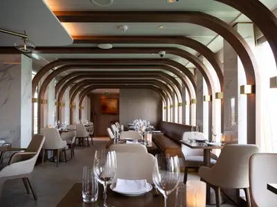 Elegantes Restaurant Onda auf der Norwegian Spirit. Holzbögen, Marmorwände, goldene Wandleuchten, gedeckte Tische mit Stühlen und Lederbank. Tageslicht. Ohne Personen.