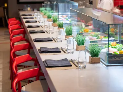 Eine elegante Sushi-Bar an Bord der Norwegian Spirit mit einer langen Theke, gedeckten Tischen und einer Vitrine mit frischen Speisen und Dekorationen.