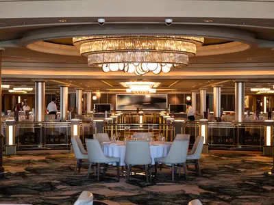Blick in das elegante Hauptrestaurant 'Taste' an Bord der Norwegian Spirit mit einem großen Kronleuchter, warmem Licht und festlich gedeckten Tischen.