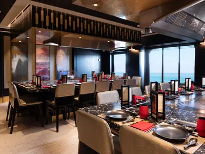 Blick in das elegant gedeckte Teppanyaki Restaurant an Bord der Norwegian Spirit mit grossen Fenstern, die einen weiten Meerblick bieten.