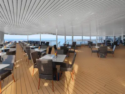 Ein weitläufiges überdachtes Buffetrestaurant an Deck der Norwegian Spirit mit vielen Tischen, Stühlen und Meerblick unter klarem Himmel.