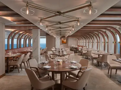 Ein elegantes Spezialitätenrestaurant namens Onda by Scarpetta an Bord der Norwegian Spirit mit modernen Holzmöbeln, Deckenlampen und Panorama-Meerblick.