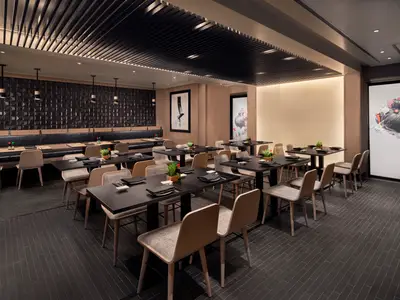 Ein leeres, elegantes asiatisches Spezialitätenrestaurant Silk an Bord der Norwegian Spirit, mit dunklen Tischen, hellen Holzstühlen und beleuchteter Kunst an den Wänden.