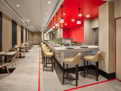 Modernes Spezialitätenrestaurant an Bord der Norwegian Spirit mit langer Sushi-Bar, Esstischen und Stühlen. Rote Decke und Wandfliesen sorgen für eine lebendige Atmosphäre. Ohne Personen.