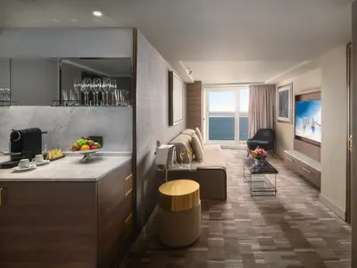 Helle Suite an Bord der Norwegian Spirit mit Wohnbereich, Balkon zum Meer, Minibar mit Obst und Kaffee, sowie einem Sofa und TV. Modernes Design in hellen Tönen.