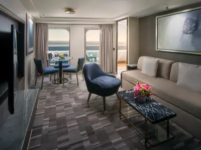 Geräumige Suite an Bord der Norwegian Spirit. Heller Wohnbereich mit Sofa, Couchtisch, Esstisch und Meerblick vom Balkon bei Sonnenuntergang.
