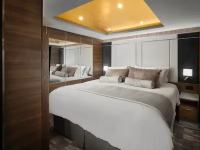 Luxuriöses Schlafzimmer an Bord der Norwegian Spirit. Grosses Doppelbett mit weisser Bettwäsche. Elegante Spiegelschränke und Holzvertäfelung. Eine goldene Decke setzt Akzente.
