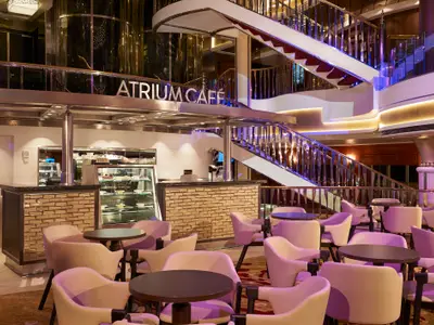 Das Atrium Café an Bord der Norwegian Star zeigt eine moderne Kaffee-Bar, lila beleuchtete Sitzbereiche und ein elegantes, geschwungenes Treppenhaus mit glänzenden Geländern.