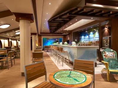 Die Margaritaville at Sea Bar an Bord der Norwegian Star zeigt eine helle Theke mit Barhockern, Tische mit Stühlen, ein tropisches Wandbild und eine dekorative Adirondack-Chair.
