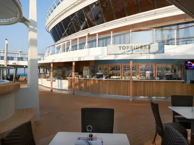 Die Topsiders Bar & Grill auf dem Sonnendeck der Norwegian Star. Eine gut bestückte Bar, Tische, Stühle und ein Whirlpool links prägen die Szene. Im Hintergrund ist das weite Meer zu sehen.