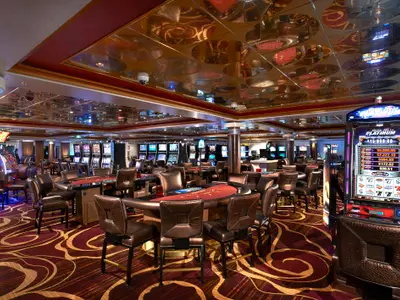 Blick in das weitlaeufige, elegant eingerichtete Casino der Norwegian Star mit Slot-Maschinen und Pokertischen. Goldene, reflektierende Decke und gemusterter Teppich.