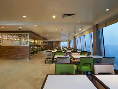 Innenansicht des Garden Cafe Buffet an Bord der Norwegian Star. Reihen von Tischen und Stühlen, links ein Buffetbereich. Fenster bieten Meerblick.