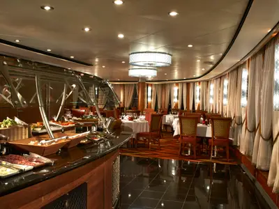 Elegantes Buffet und Speisesaal der Norwegian Star. Reichhaltiges Buffet, Tische mit roten Stühlen und helle Vorhänge an der Fensterfront. Warme Abendstimmung.