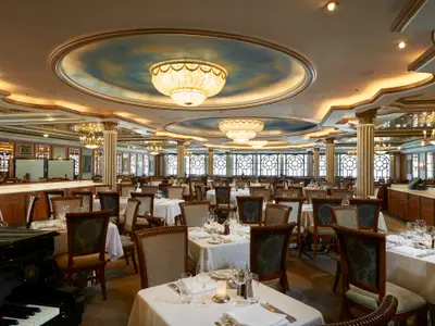 Blick in das elegante Restaurant Versailles an Bord der Norwegian Star. Zahlreiche gedeckte Tische, Kronleuchter und runde Fenster prägen den Raum.