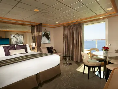 Geräumige Balkonsuite an Bord der Norwegian Star. Ein großes Doppelbett, ein Sofa, ein Esstisch und eine Veranda mit Meerblick sind zu sehen.
