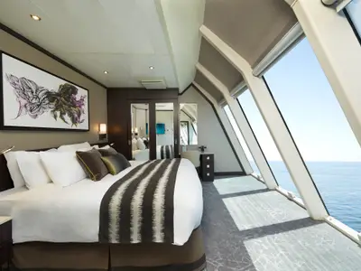 Eine geräumige, elegant eingerichtete Suite an Bord der Norwegian Star. Ein grosses Bett, ein Schreibtisch und wandhohe Fenster mit Blick auf das offene Meer sind zu sehen.