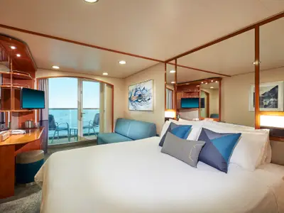Balkonkabine an Bord der Norwegian Sun mit großem Bett, blauem Sofa, Schreibtischbereich und Balkon mit Meerblick. Das Zimmer ist hell und modern eingerichtet.