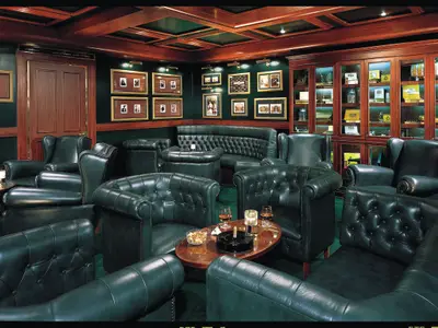 Luxuriöse Churchill's Cigar Bar der Norwegian Sun. Dunkelgrüne Leder-Möbel, Holzvertäfelung, gerahmte Bilder, Zigarrenvitrinen. Tische mit Drinks.