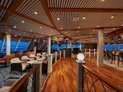 Blick in die Spinnaker Lounge der Norwegian Sun am Abend. Die stilvolle Lounge zeigt eine Bar, einen Tanzbereich und zahlreiche bequeme Sessel.