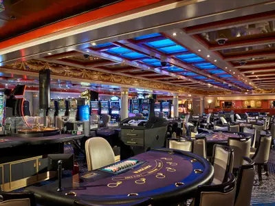 Blick in das Sun Casino an Bord der Norwegian Sun mit Reihen von Spielautomaten und mehreren Spieltischen. Der Raum ist hell beleuchtet.