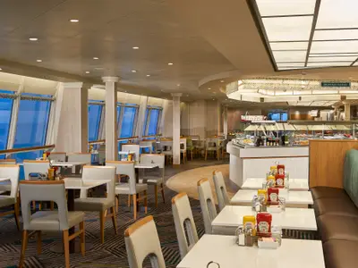 Blick in das Buffetrestaurant Sun Garden Cafe an Bord der Norwegian Sun. Tische, Stühle und eine Buffettheke sind sichtbar. Grosse Fensterfronten bieten weiten Meerblick.