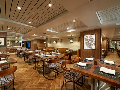 Spezialitätenrestaurant Los Lobos an Bord der Norwegian Sun. Holzwände, Ledersitzbänke, gemusterte Stühle und gedeckte Tische. Kunst an den Wänden.