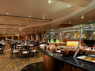 Umfassendes Buffetrestaurant an Bord der Norwegian Sun, das eine vielfältige Auswahl an Speisen wie Salate, Käse und Aufschnitt präsentiert. Im Hintergrund sind zahlreiche elegant gedeckte Tische in einem weitläufigen Speisesaal zu sehen. Die Beleuchtung ist warm und einladend.