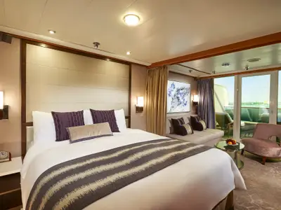 Helle, elegante Suite an Bord der Norwegian Sun mit Doppelbett, Sitzbereich und Balkon mit Meerblick. Die Einrichtung zeigt Lila- und Beigetöne.