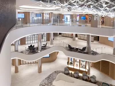 Blick von oben in das helle, mehrstöckige Atrium der Norwegian Viva mit geschwungenen Balustraden aus Glas und Weiß, luxuriösen Geschäften und komfortablen Sitzgruppen auf verschiedenen Ebenen.