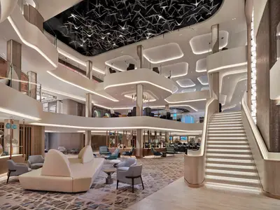 Das mehrstöckige Penrose Atrium an Bord der Norwegian Viva zeigt elegante Lounge-Bereiche, eine beleuchtete Treppe und eine moderne Deckeninstallation.