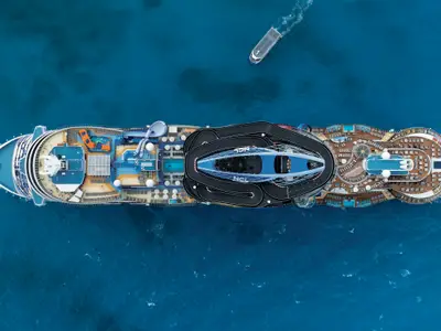 Luftaufnahme der Norwegian Viva. Das Oberdeck bietet eine Go-Kart-Bahn, Pools und bunte Wasserrutschen. Ein Beiboot fährt im blauen Meer.