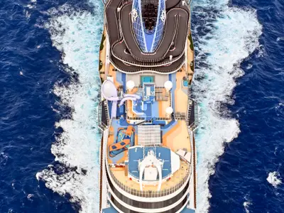 Luftaufnahme des Kreuzfahrtschiffs Norwegian Viva, das durch blaues Meer fährt. Auf dem Oberdeck sind eine markante, mehrstöckige Gokart-Bahn und ein farbenfroher Aqua Park mit Wasserrutschen und Pools zu sehen.